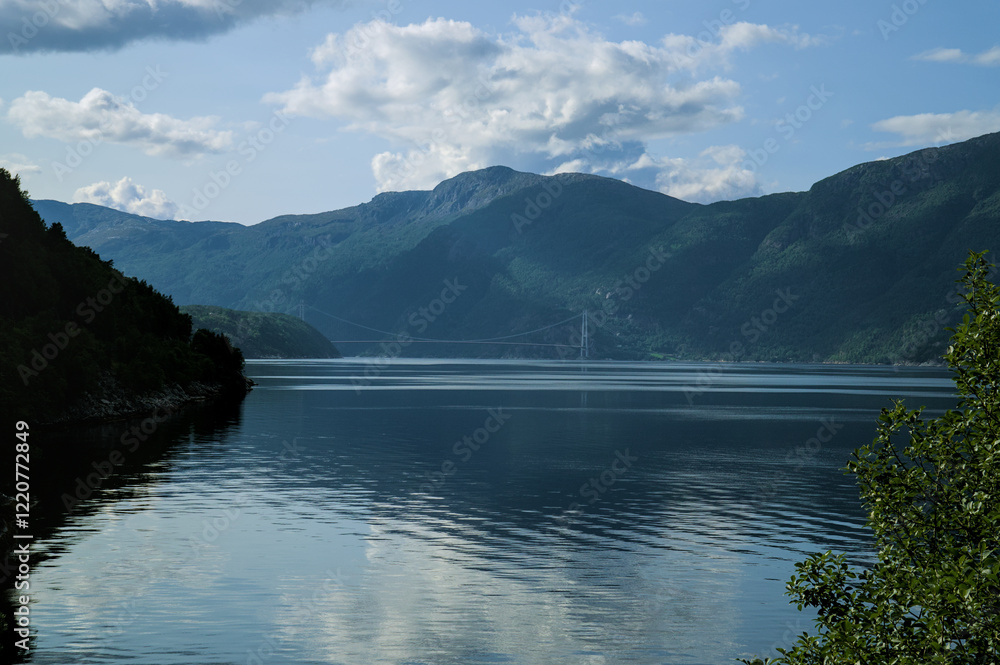 Fjord surrounded by lush green mountains, with a suspension bridge in the distance. Fjord surrounded by lush green mountains, with a suspension bridge in the distance.