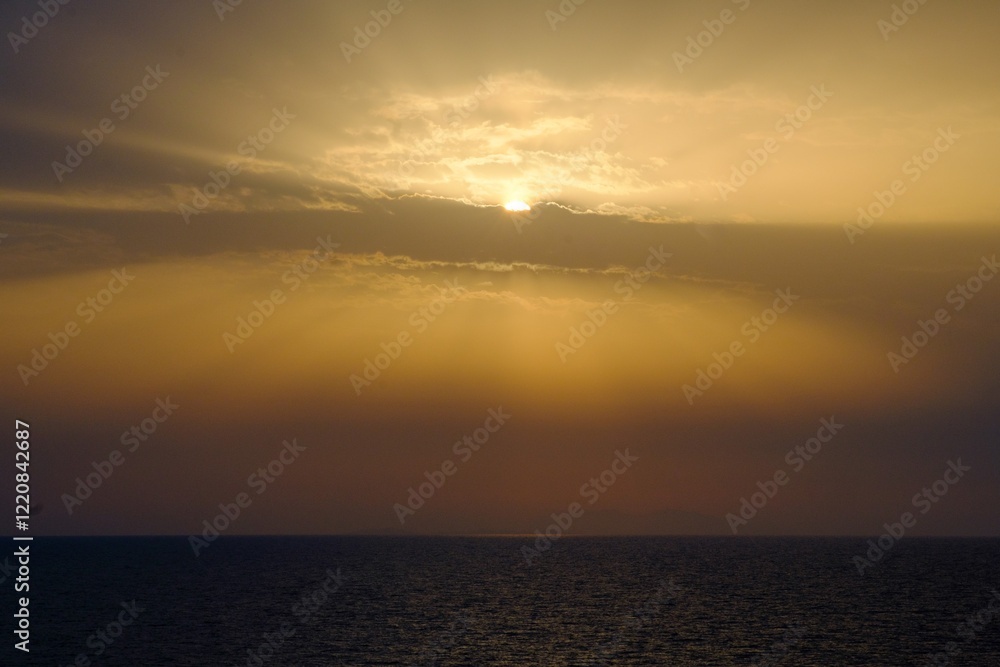 Obraz premium The sun shines brilliantly through clouds above the ocean at sunset