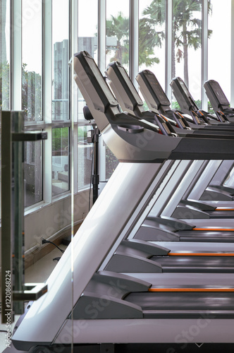 Perspective view of Treadmill in the morning with sunlight shines through the glass into fitness room. Side view of Treadmill machines at gym, use it as your Wallpaper, Poster and Copy space,