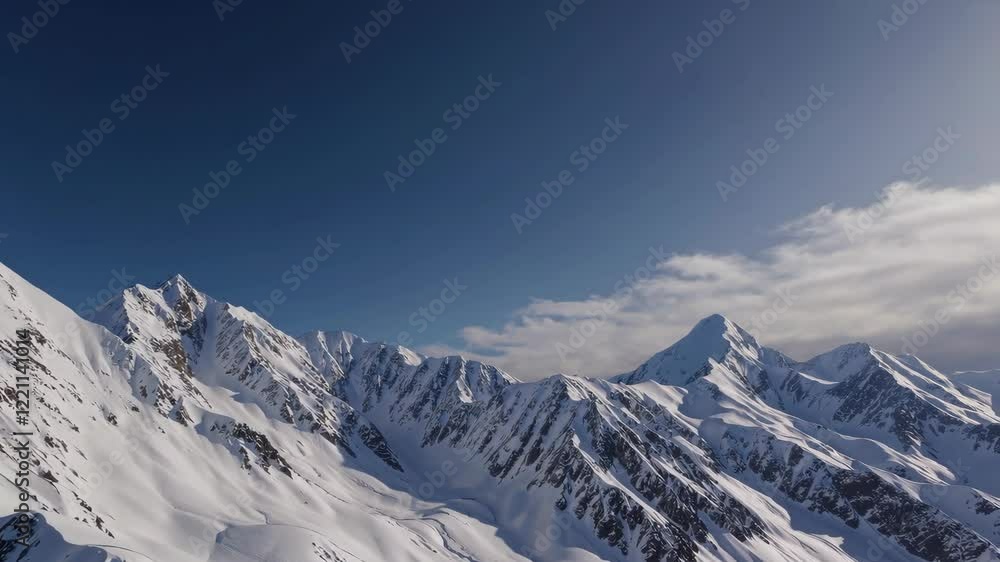 Snow-covered mountains under a clear blue sky with soft clouds Snow-covered mountains under a clear blue sky with soft clouds