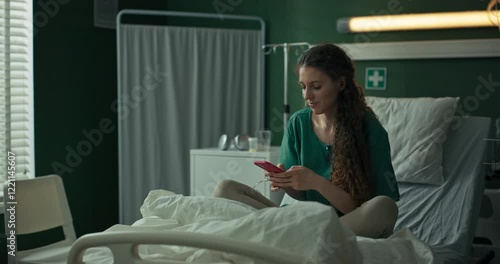 Young patient sits on her hospital bed, focused on her phone as she types a message.
