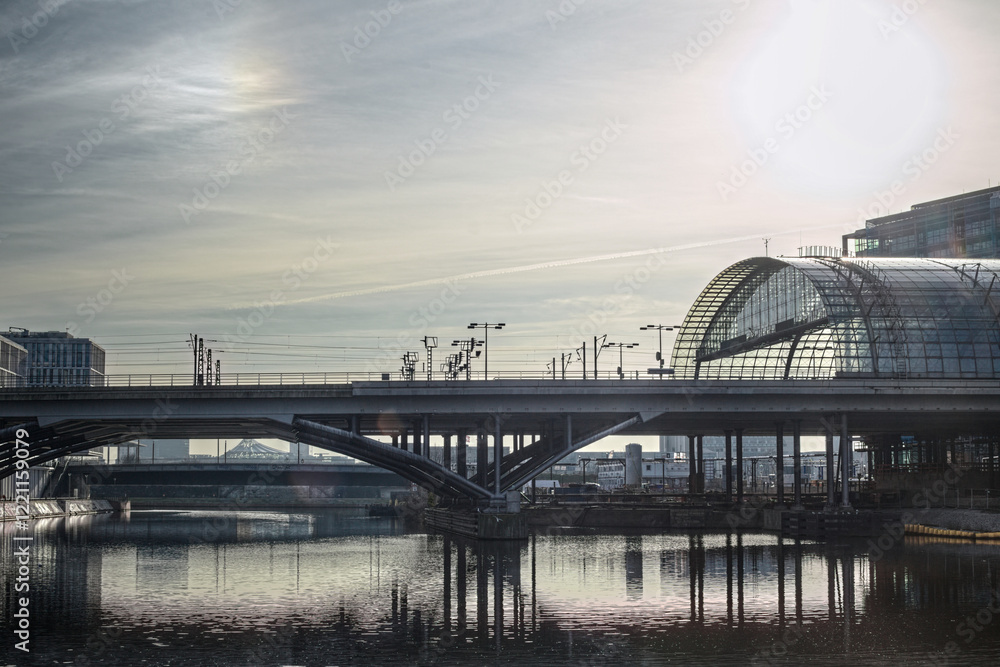 Naklejka premium Bridge and reflections at Berlin Central Station under soft sunlight over a calm urban river scene