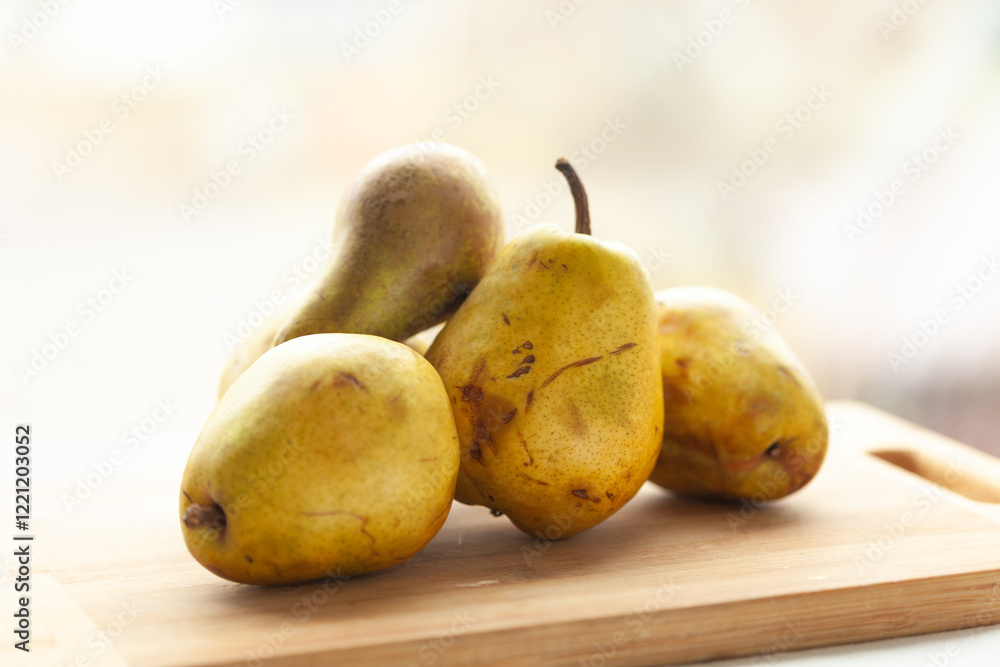 Four ripe pears rest on a light wooden cutting board, bathed in soft, natural light. Four ripe pears rest on a light wooden cutting board, bathed in soft, natural light.