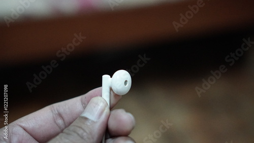 a person's finger holding an earphone, in a blurred background