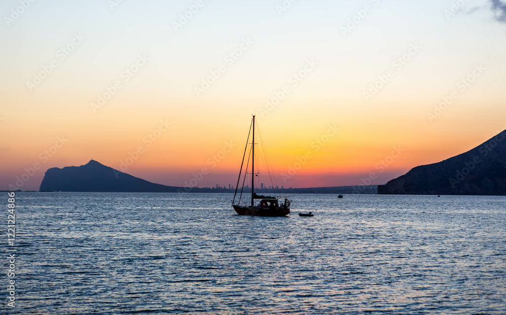 Fototapeta premium Sailboat view at sunset over Benidorm town in the province of Alicante, Valencian Community, Spain. Mediterranean sea coast in Costa Blanca region.