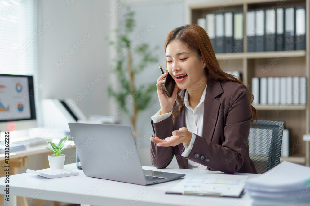 Asian businesswoman talking on mobile phone and working on laptop in office Asian businesswoman talking on mobile phone and working on laptop in office
