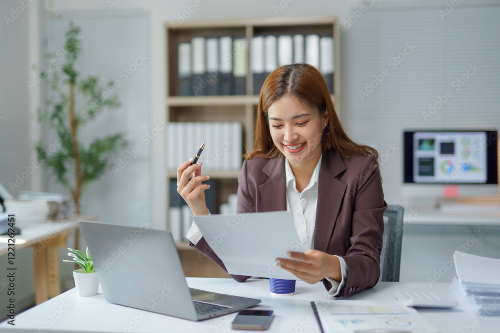 Asian businesswoman smiling and reading a document at office desk Asian businesswoman smiling and reading a document at office desk