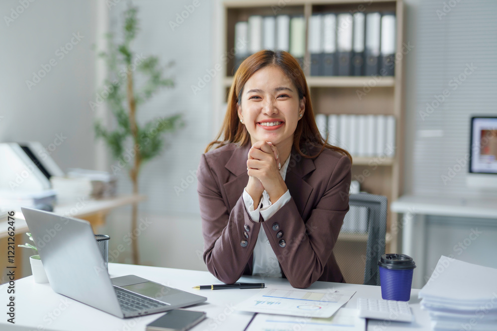 Smiling businesswoman sitting at desk with laptop and documents, working in modern office Smiling businesswoman sitting at desk with laptop and documents, working in modern office