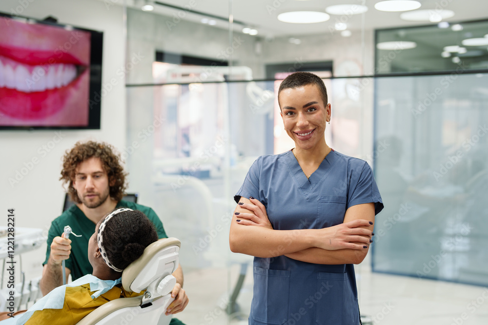 Obraz premium Smiling Caucasian female dental assistant in a contemporary clinic, wearing a blue scrub. A diverse team works on a patient, ensuring comfort. The setting is bright and professional.