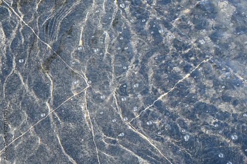 A thin layer of water with ripples on dark marble fountain tiles, illuminated by sunlight. Texture in full screen.