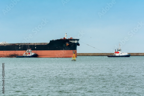 Grand navire en train de sortir du port de Dunkerque et aidé par des bateaux remorqueurs photo