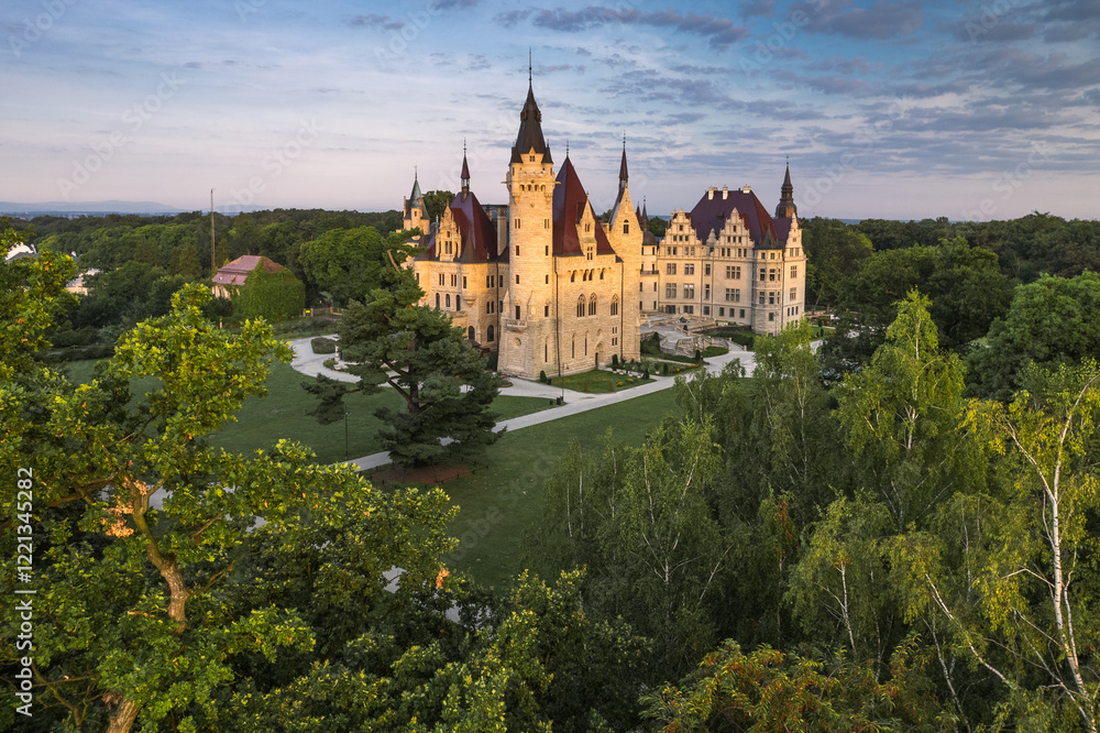 Majestic Moszna Castle on a warm summer morning, surrounded by lush greenery and glowing in soft golden sunlight, reflecting a fairytale-like ambiance perfect for travel and architecture themes.