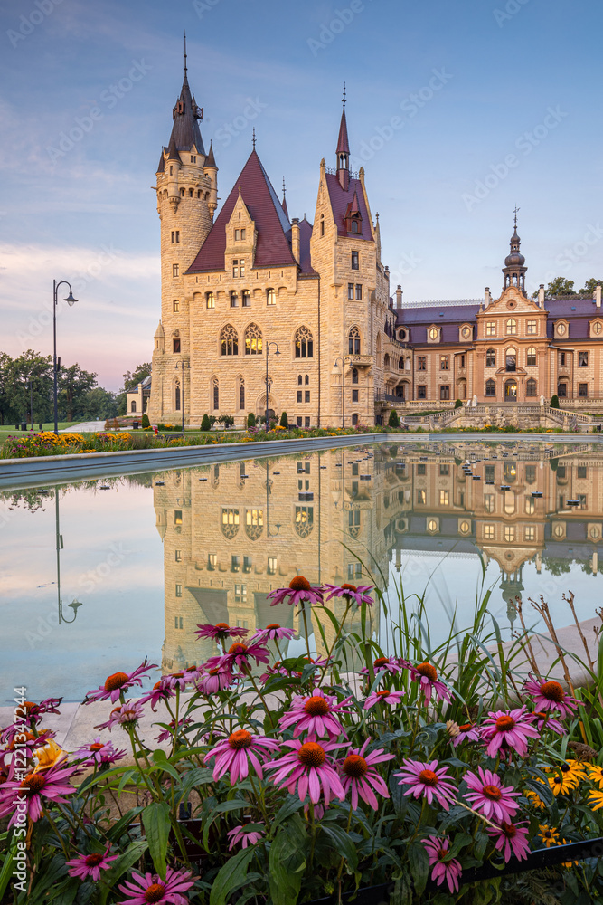 Majestic Moszna Castle on a warm summer morning, surrounded by lush greenery and glowing in soft golden sunlight, reflecting a fairytale-like ambiance perfect for travel and architecture themes.