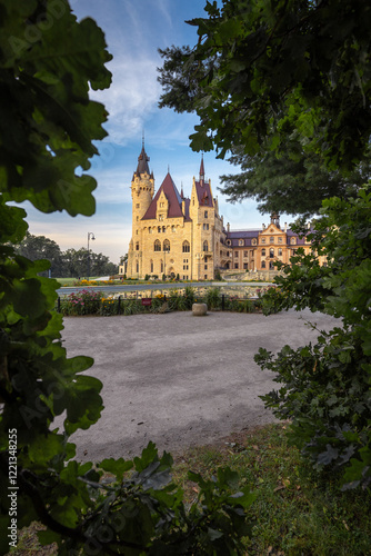Obraz na płótnie Majestic Moszna Castle on a warm summer morning, surrounded by lush greenery and glowing in soft golden sunlight, reflecting a fairytale-like ambiance perfect for travel and architecture themes. w salonie