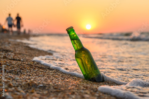 Bottle of beer on the beach with vacationers in the background. Beer by the sea with sunset in the background. photo