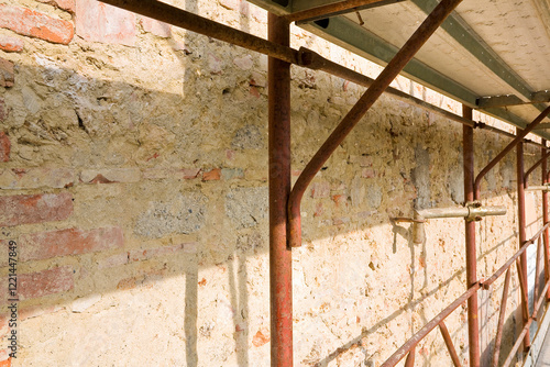 REMOVING OLD PLASTER FROM A STONE AND BRICK WALL - Construction work on a building site with security metal scaffolding for protection against falls photo