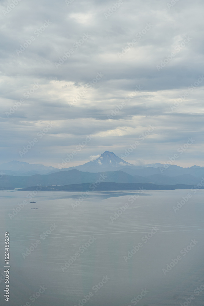 A breathtakingly stunning view of a majestic Vilyuchinsky volcano in Kamchatka silhouetted gracefully against a tranquil lake and overcast sky