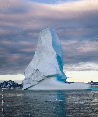 Iceberg in Greenland. Colorful huge Iceberg building. Large ice block floating in the ocean. The sky is cloudy and the sun is setting