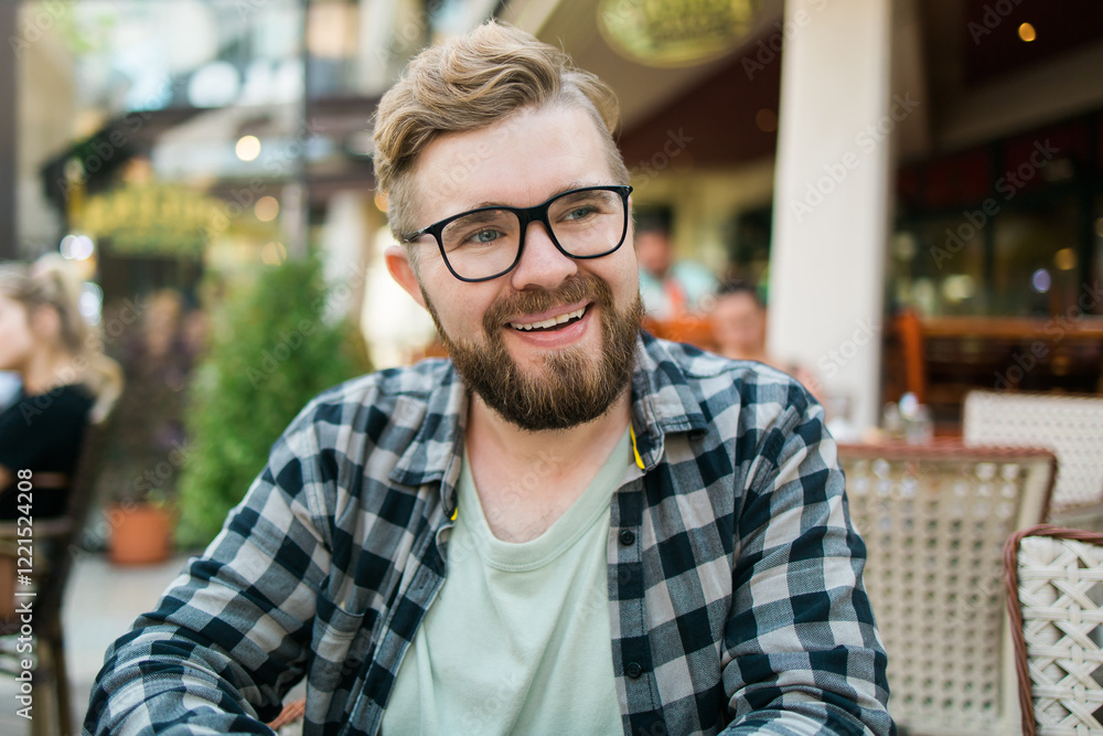 Bearded man in glasses laughing joyfully while sitting at a cafe table outdoors. Bearded man in glasses laughing joyfully while sitting at a cafe table outdoors.