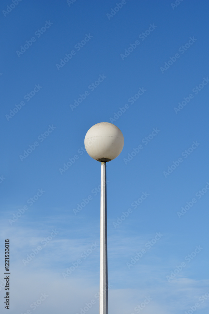 A tall white street lamp with a round globe against a blue sky A tall white street lamp with a round globe against a blue sky