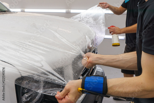 A worker is applying transparent film to a car to protect it from gravel and scratches on the hood of a white car. Applying transparent paint protection film