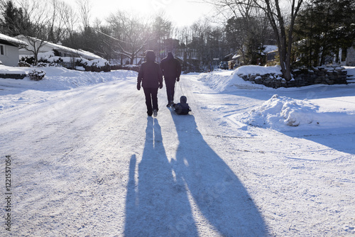 Fotografi Horizontal backlit view of unrecognizable couple hauling child in sledge on stre