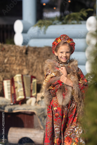 A blonde girl in a national Russian costume on the Maslenitsa holiday. A beautiful russian girl in a national costume made of a fur cape and kokoshnik on the background of a hayloft. 
