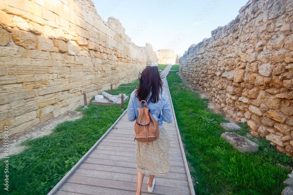 A woman tourist with a backpack walks and examines the ruins of an ancient city. Khersones, Sevastopol, Crimea.