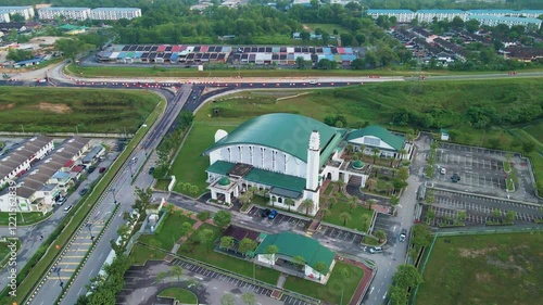 4K aerial view of Masjid Perodua, Bukit Beruntung, surrounded by housing, roads, and greenery, featuring a green roof and spacious parking. photo