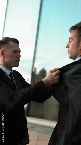 Angry Young businessman grabbing his colleague by the lapels of suite. He want to start fighting. Hard conversation and debate. Glossy business-centre building sunset at the background. Teal and