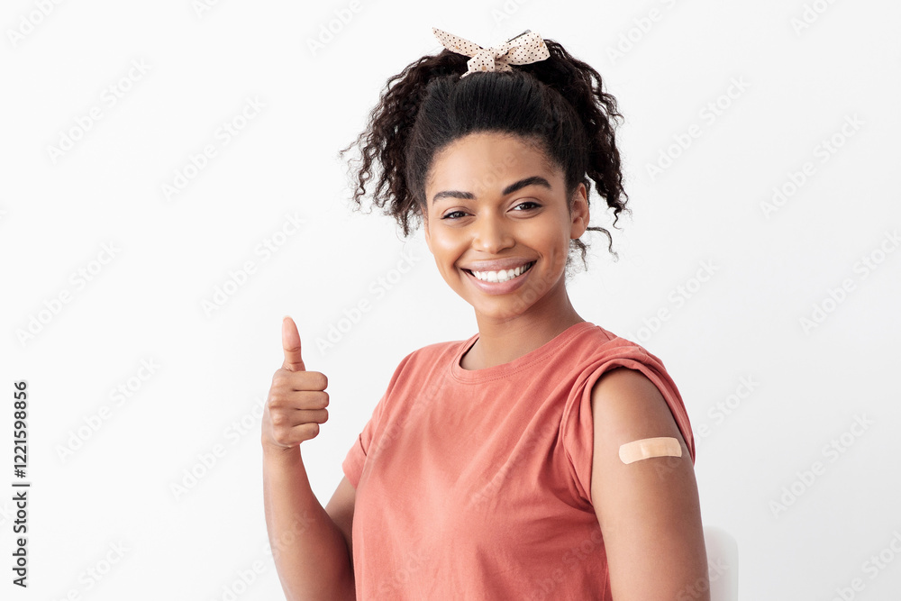 Cheerful african american lady patient showing thumb up and smiling at camera, got vaccinated against coronavirus, having adhesive medical band on her shoulder, studio background, panorama, copy space Cheerful african american lady patient showing thumb up and smiling at camera, got vaccinated against coronavirus, having adhesive medical band on her shoulder, studio background, panorama, copy space