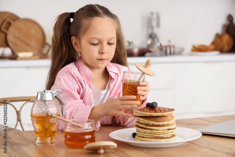 Cute little girl with honey and pancakes at table in kitchen Cute little girl with honey and pancakes at table in kitchen