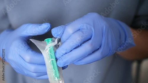 Healthcare worker wearing protective blue gloves prepares sterile syringe, focusing on safe medical injection protocol while ensuring precise handling of sterile syringe and medical equipment. 