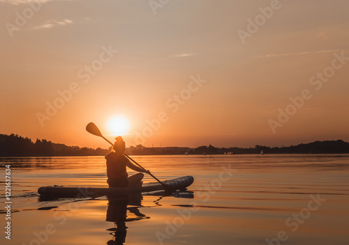 Obraz na płótnie Sunlit silhouette of a women paddling sitting on a standup paddleboarding (SUP) desk. Scenic sunset landscape view at Kiekrz lake (Jezioro Kierskie) near Poznań, Wielkopolskie, Poland. w salonie