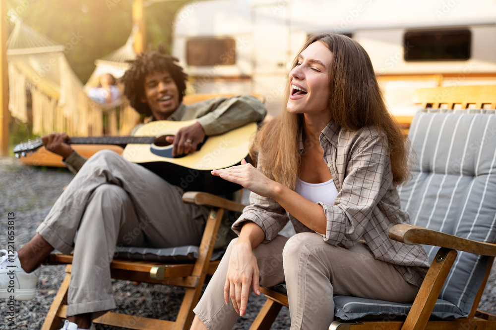 Carefree diverse friends singing and playing guitar, enjoying music near RV on camping trip. Young lady and black guy having fun on summer holidays, spending time in nature Carefree diverse friends singing and playing guitar, enjoying music near RV on camping trip. Young lady and black guy having fun on summer holidays, spending time in nature