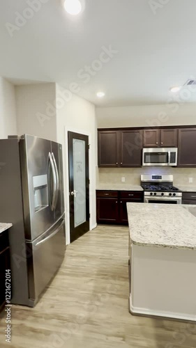 modern kitchen in open concept house with stainless steel appliances, white countertops and brown cabinetry.