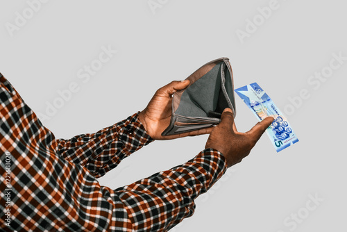 Black hands Holding empty opened men wallet With a single five Ghanaian cedi note in hand removing money out of wallet. no money poor person concept  photo