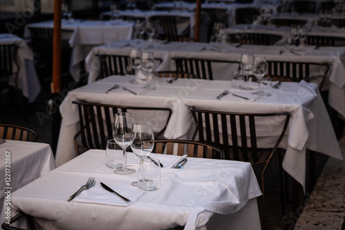 Photography Neatly set tables with white linens stand ready at an open-air Italian restaurant in central Rome