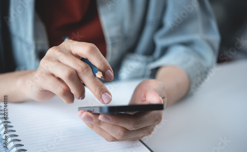 Woman using mobile phone with notebook on office table. Business woman surfing the internet, searching the information on smartphone working at workplace, close up photo