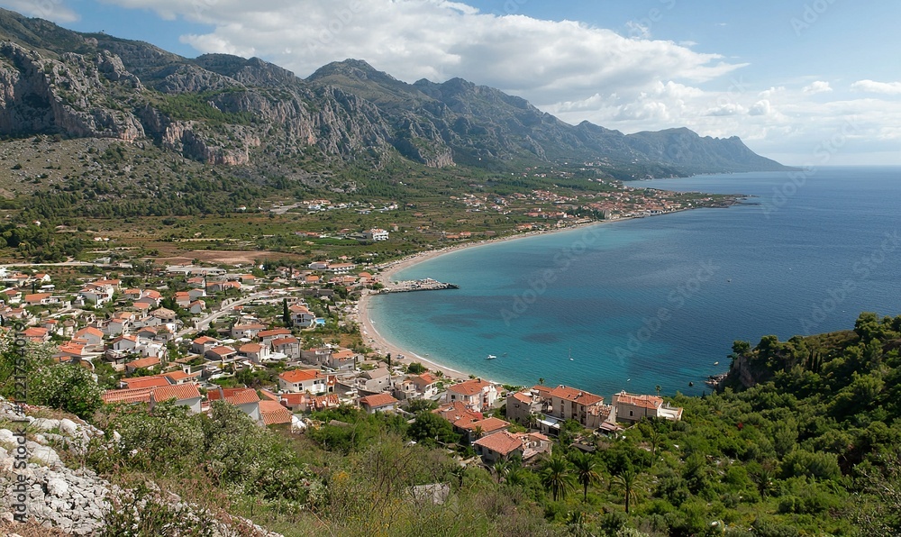 Fototapeta premium Coastal town nestled beneath mountains, serene bay view, ideal for travel or tourism promotion