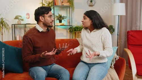 Upset young Indian couple in casual clothes arguing fighting while sitting on sofa in living room at home. Diverse disappointed girlfriend and boyfriend shouting at each other on couch in apartment.