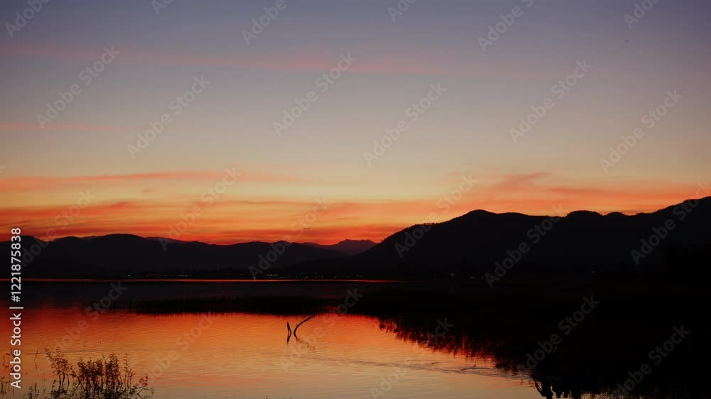 Serene evening at lake, where sunset paints sky in vibrant hues, reflecting on water, with silhouettes of mountains creating tranquil nature scene. Timelapse Cloud Landscape 4K Serene evening at lake, where sunset paints sky in vibrant hues, reflecting on water, with silhouettes of mountains creating tranquil nature scene. Timelapse Cloud Landscape 4K