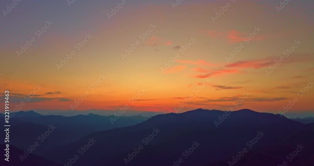 Aerial view of A breathtaking view of a colorful sunset over layered mountain silhouettes, with warm hues of orange, pink, and blue blending seamlessly across the sky. Aerial view of A breathtaking view of a colorful sunset over layered mountain silhouettes, with warm hues of orange, pink, and blue blending seamlessly across the sky.