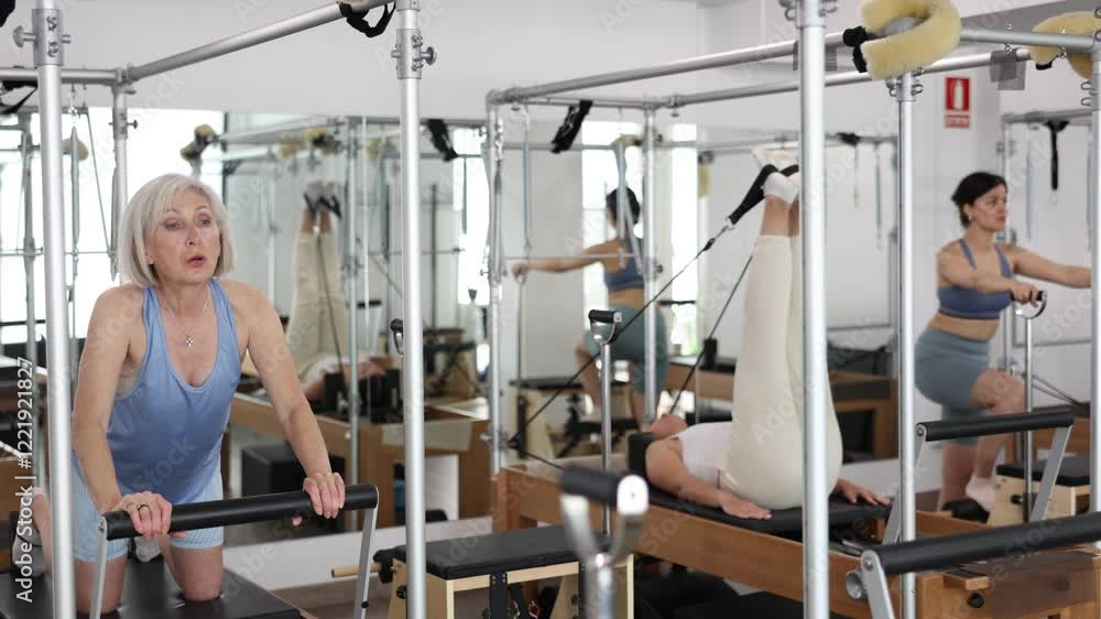 Mature woman doing lower back exercises while lying on Pilates bed in wellness center. High quality 4k footage Mature woman doing lower back exercises while lying on Pilates bed in wellness center. High quality 4k footage