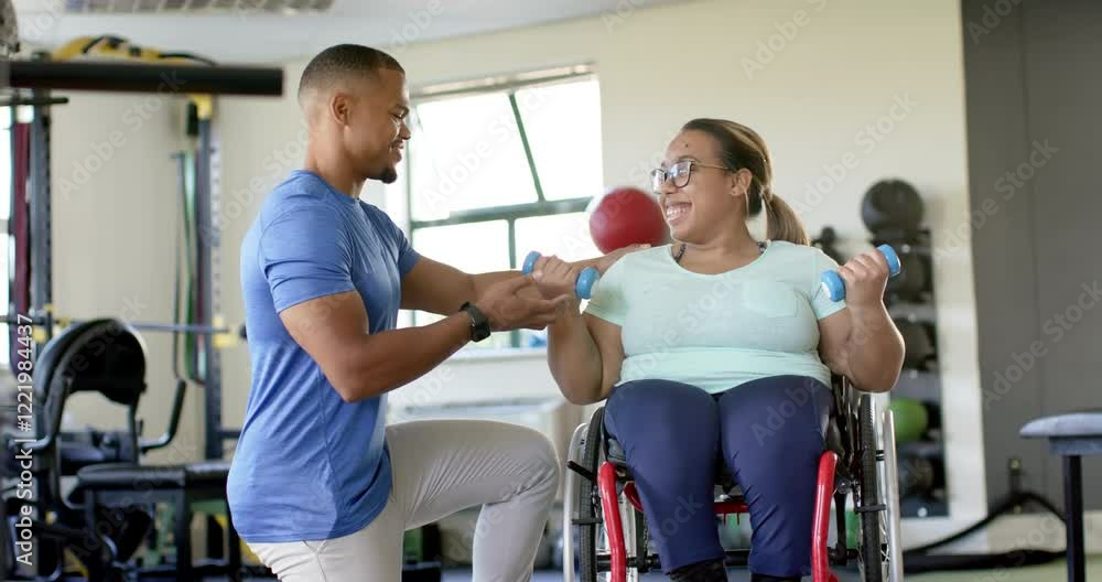 Assisting woman with paraplegia in wheelchair, therapist guiding exercise with dumbbells in rehab Assisting woman with paraplegia in wheelchair, therapist guiding exercise with dumbbells in rehab