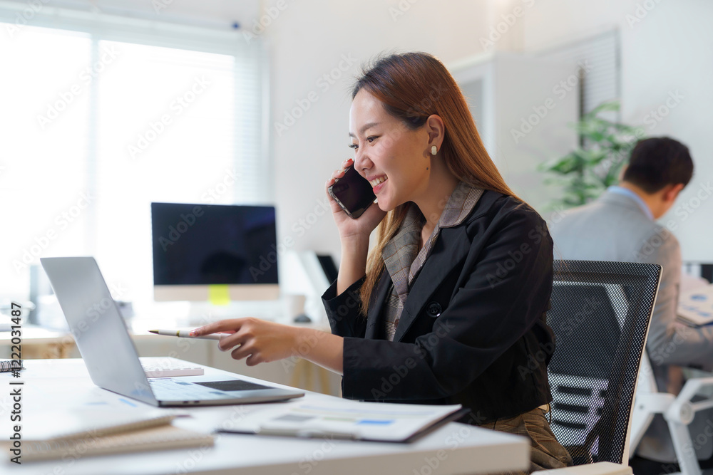 Asian businesswoman talking on phone and working on laptop in modern office Asian businesswoman talking on phone and working on laptop in modern office