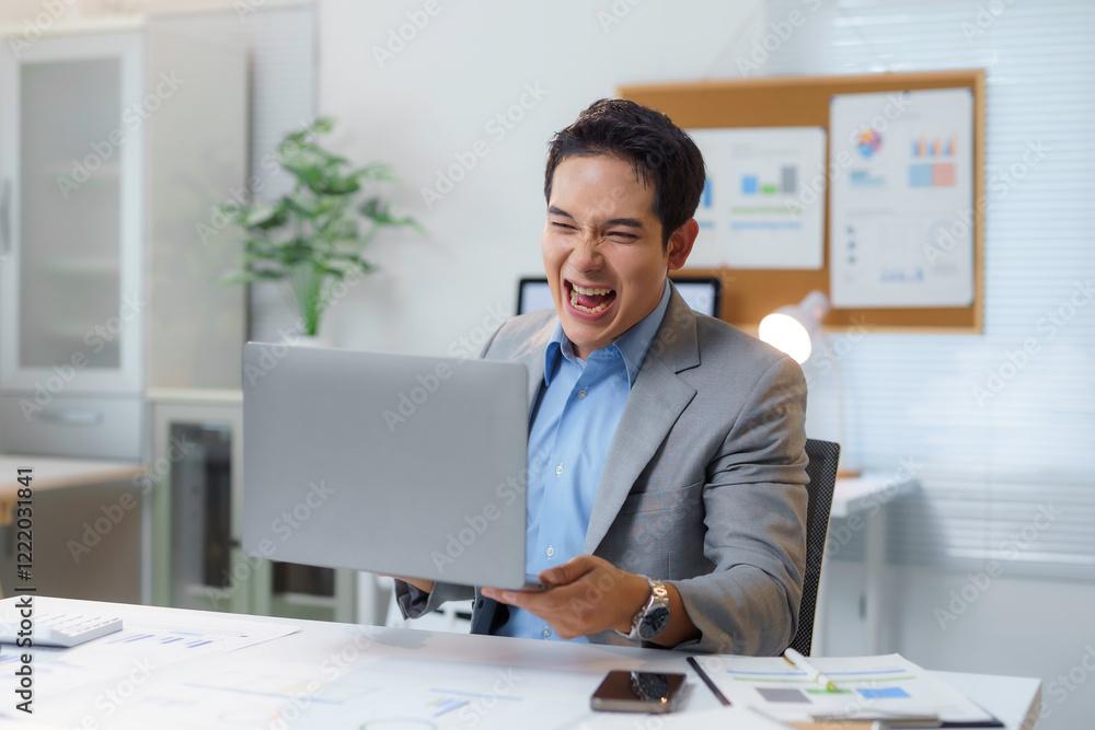 Excited Asian businessman celebrating success while holding laptop in office Excited Asian businessman celebrating success while holding laptop in office