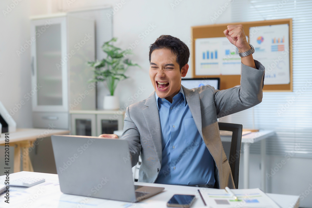 Naklejka premium Excited businessman celebrating success while working on laptop in office