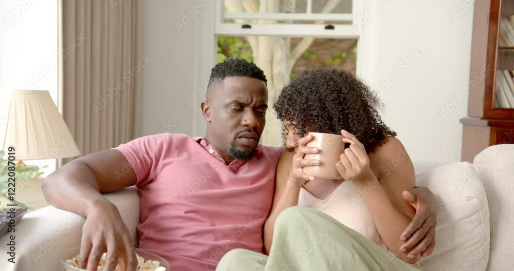 Sitting on couch, couple sharing popcorn and drinking coffee, enjoying time together Sitting on couch, couple sharing popcorn and drinking coffee, enjoying time together