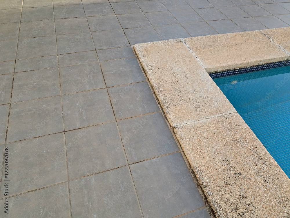 Fototapeta premium Minimalist poolside corner with gravel washed stone and concrete slabs, textured edge and grey detroit tiled flooring. Serene summery atmosphere for outdoor relaxation.